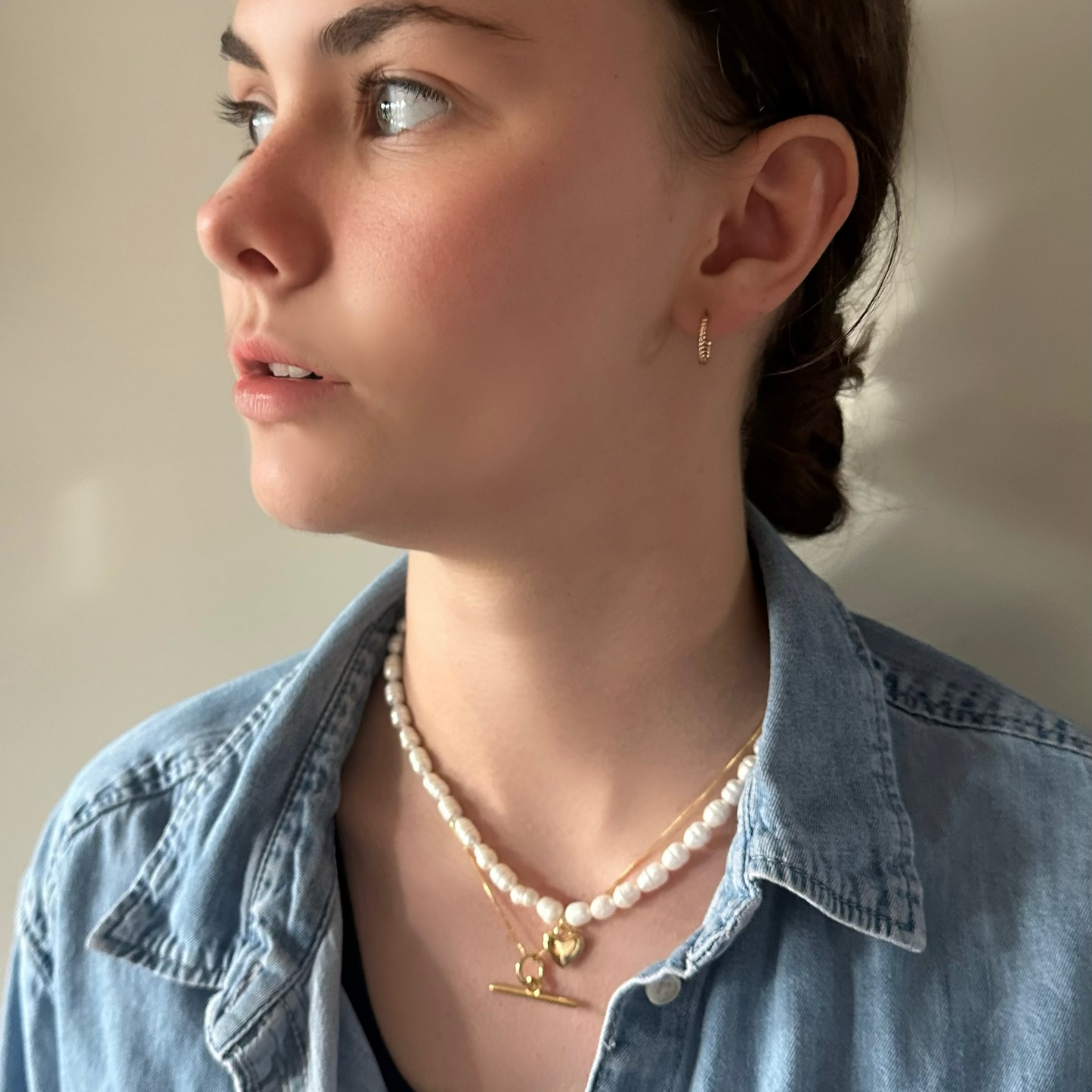 Woman wearing a denim jacket and pearl necklace with a neutral background