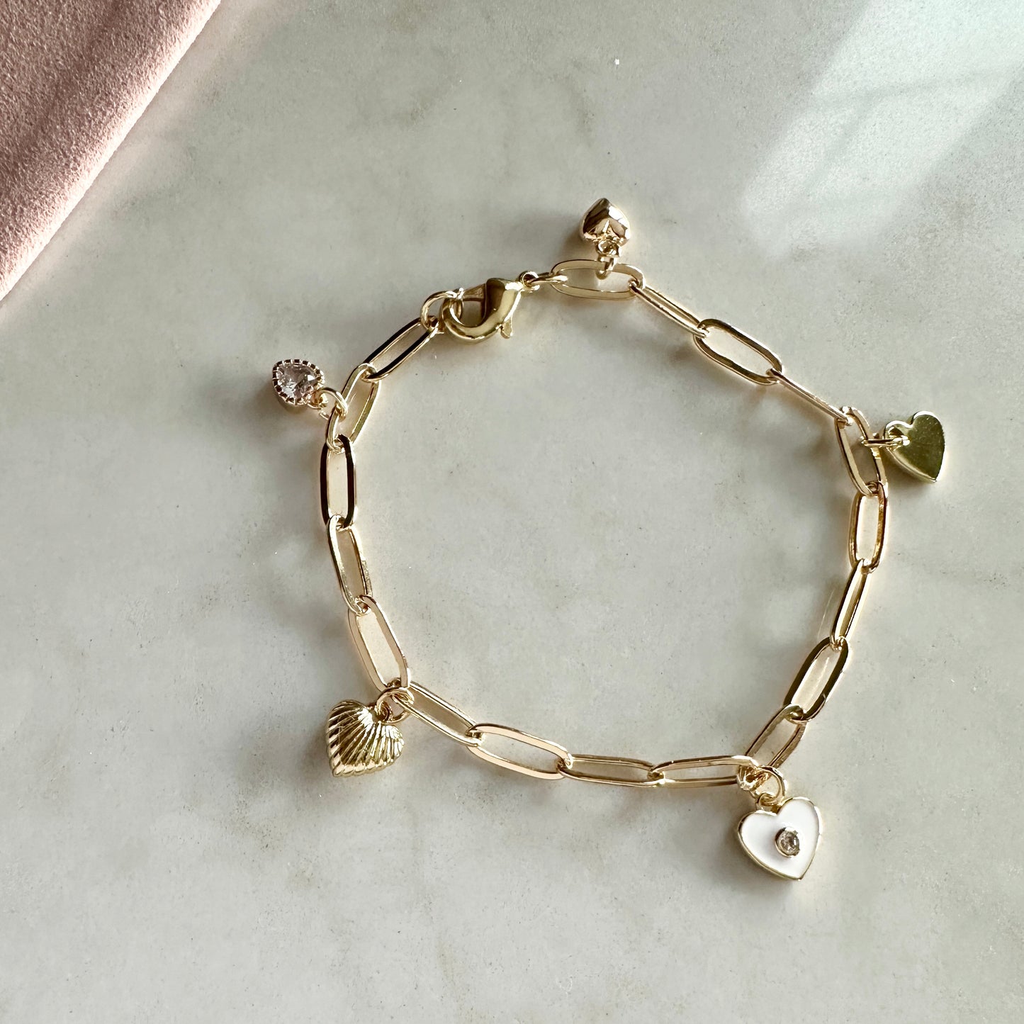 Gold chain bracelet with heart and shell charms on a marble surface