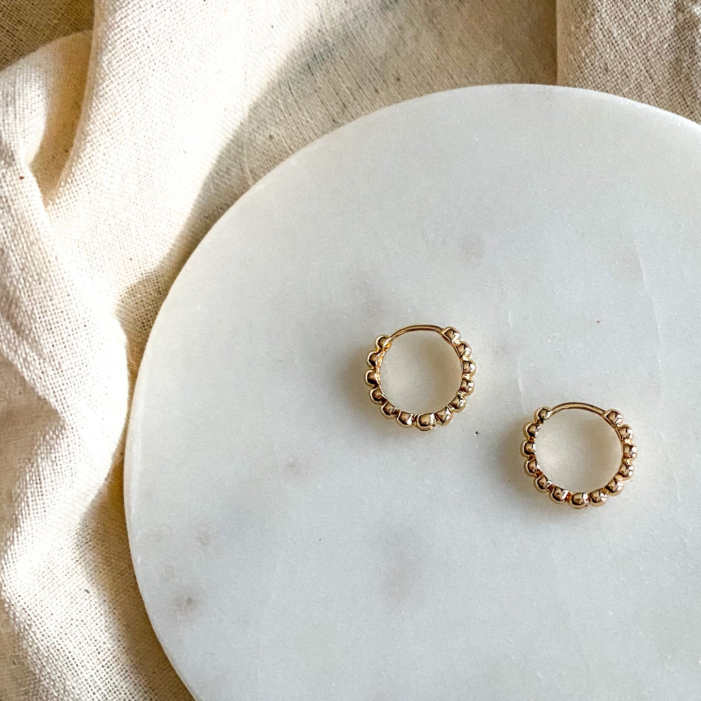A pair of gold hoop earrings with a textured design, placed on a white marble surface.