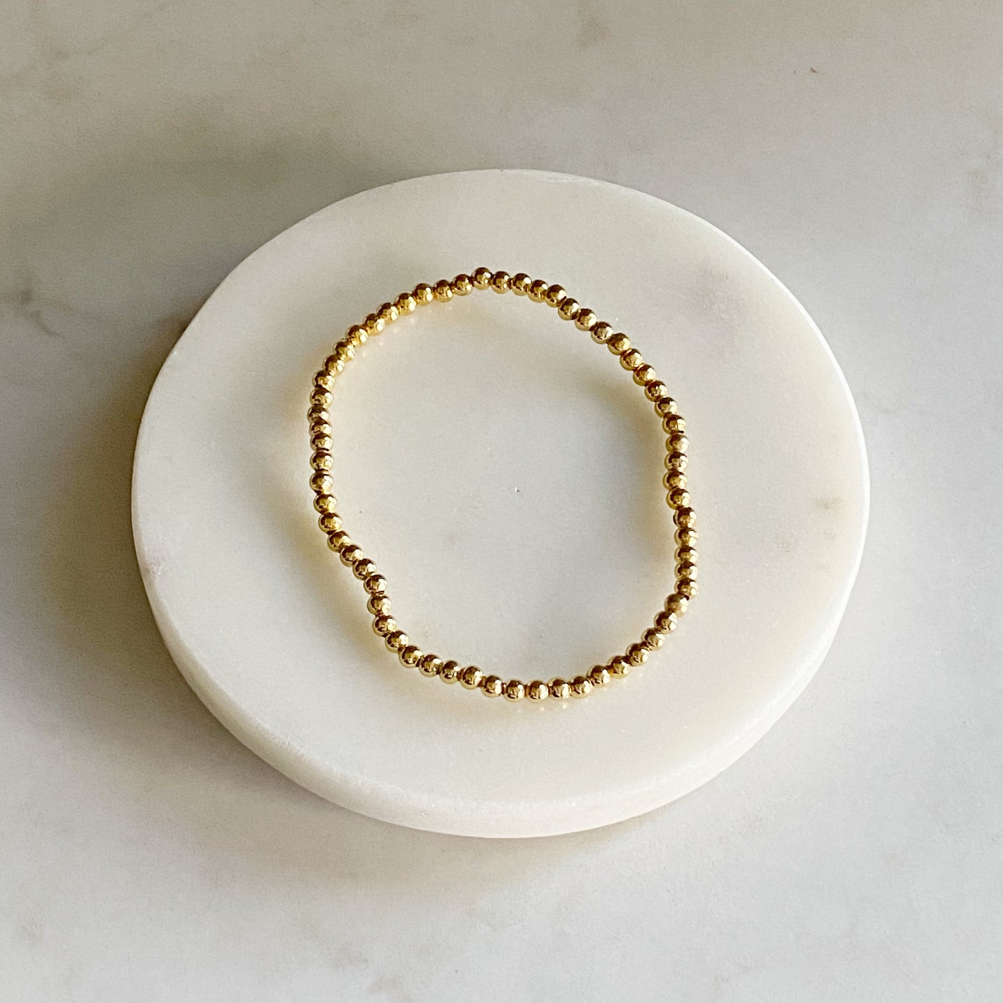 A gold beaded bracelet with a shiny finish displayed on a white surface.
