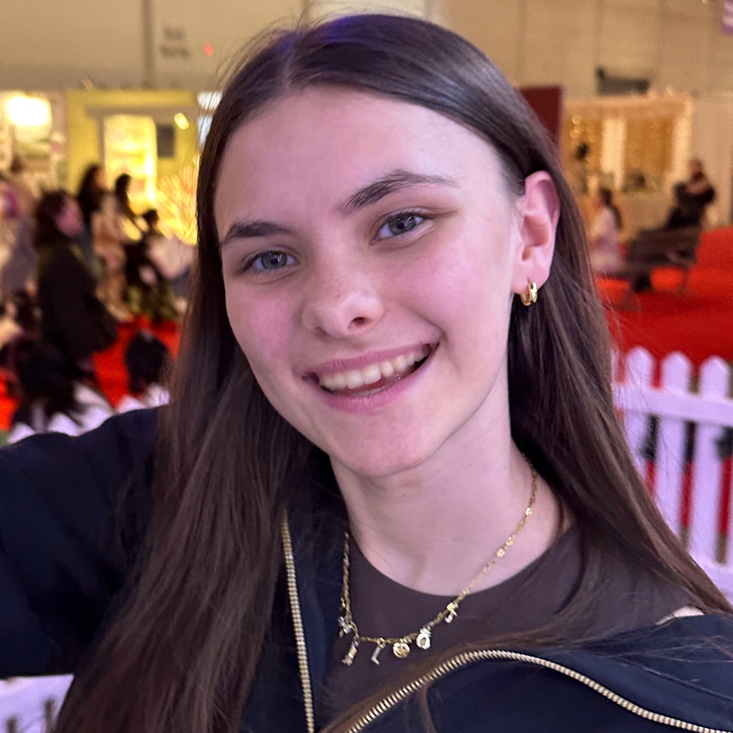 Woman with long brown hair smiling at a blurred indoor event background