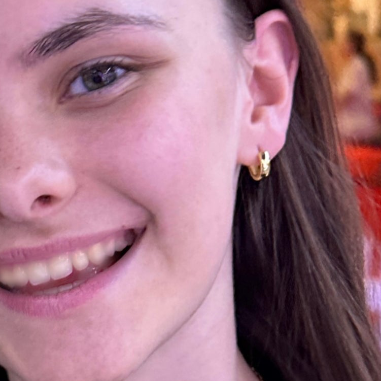 Close-up of a person wearing a gold hoop earring with a blurred background