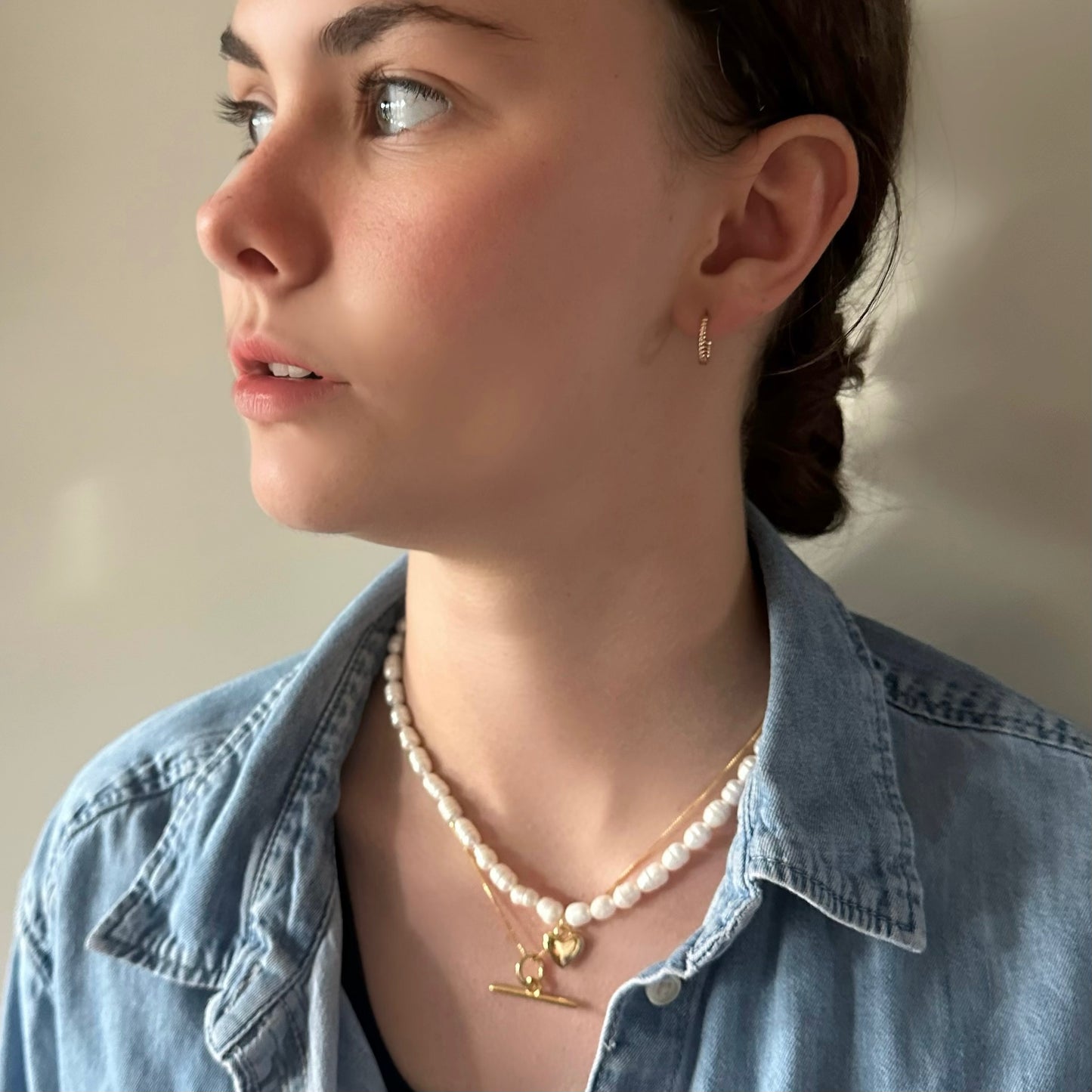Woman wearing a pearl necklace and gold earrings against a neutral background