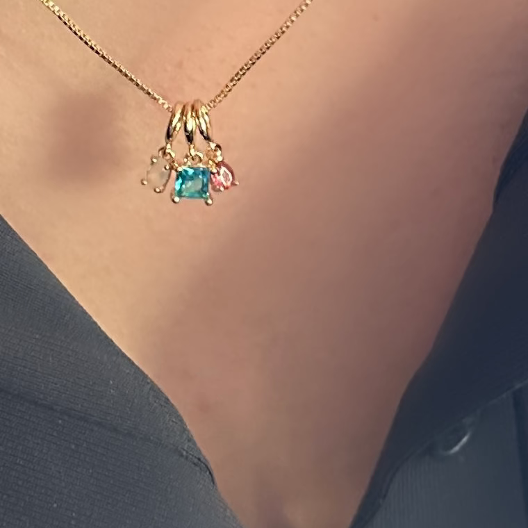 A close-up of a gold chain necklace worn on a person's neck, featuring a small pendant with a blue-green center stone and tiny accent stones.