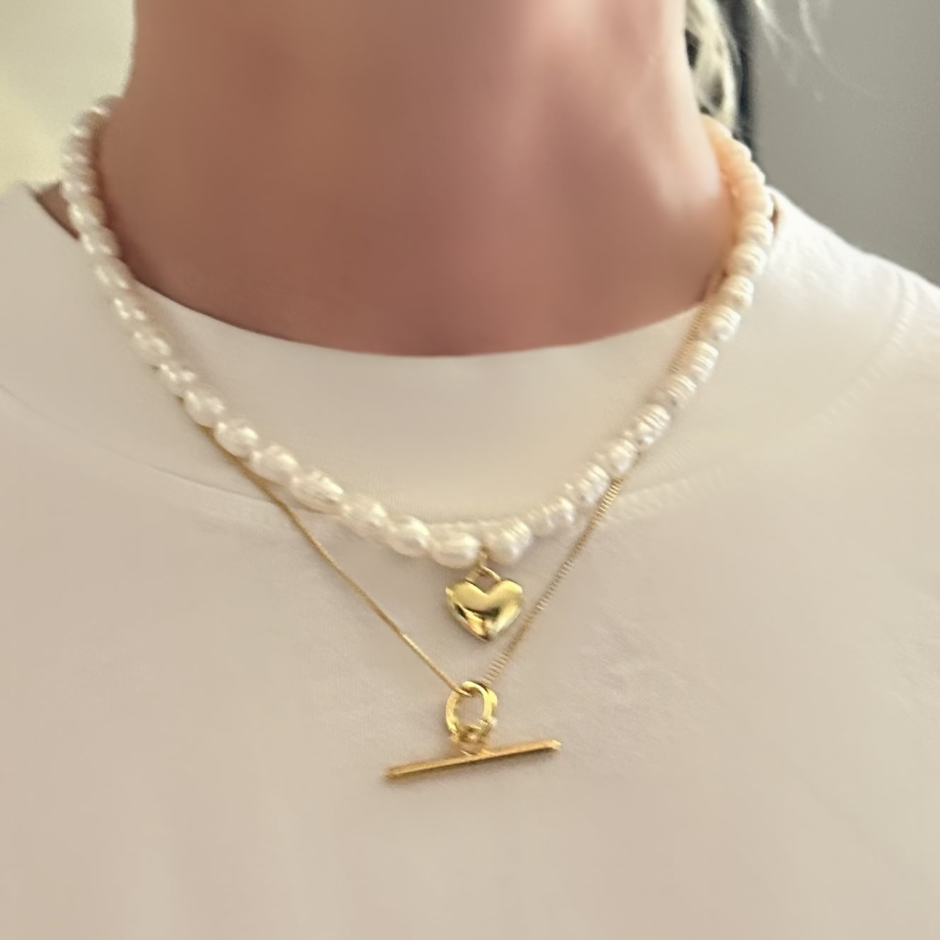 Pearl necklace with gold clasp and heart pendant on a plain background