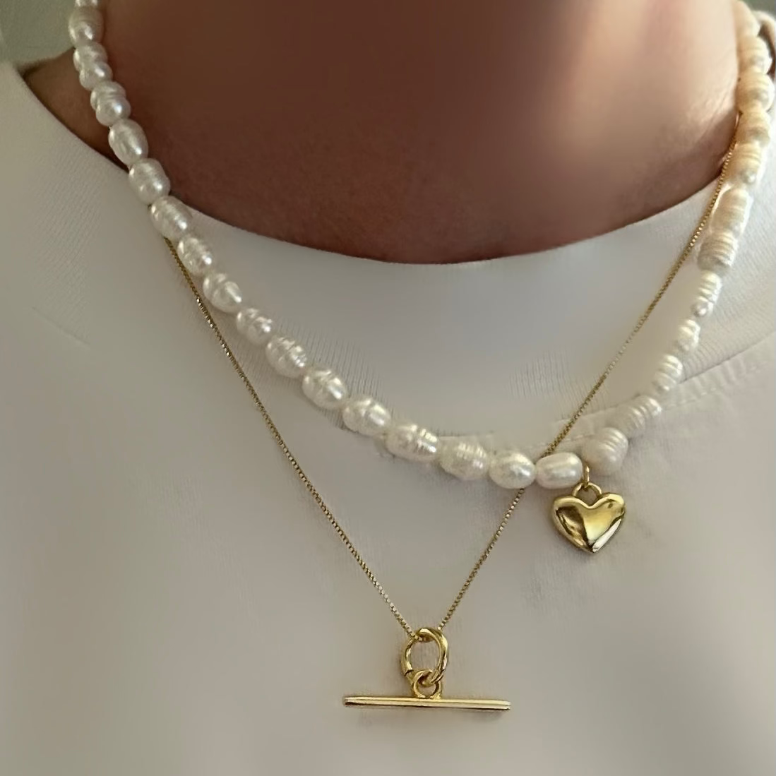 Two necklaces with heart and bar pendants on a plain background