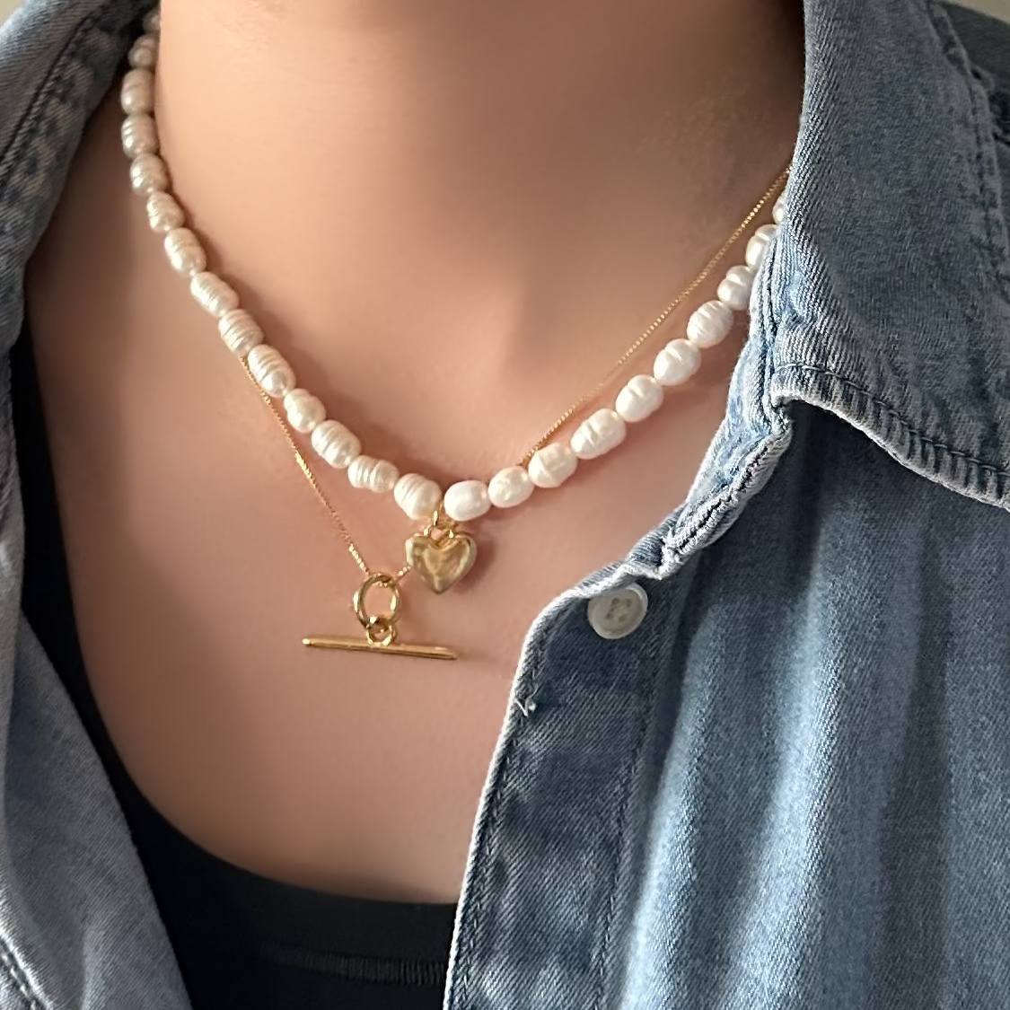 Necklace with heart and T-bar pendants on a mannequin wearing a denim jacket.