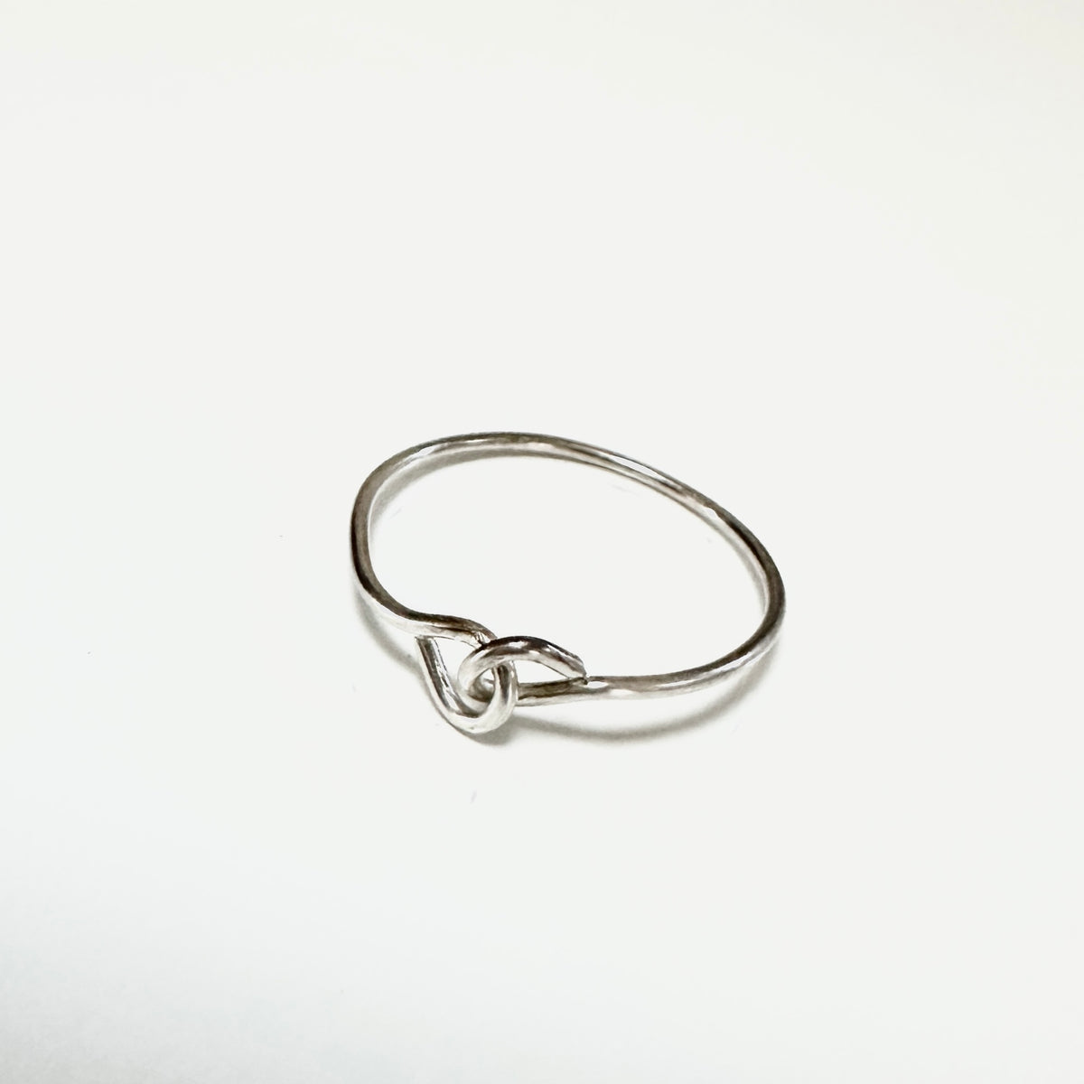 A minimalist sterling silver ring with a small heart-shaped knot detail at the center, displayed on a clean white background.