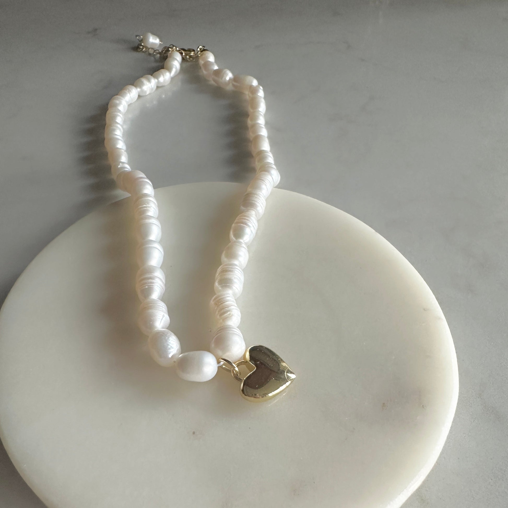 Pearl necklace with a gold heart charm on a white dish
