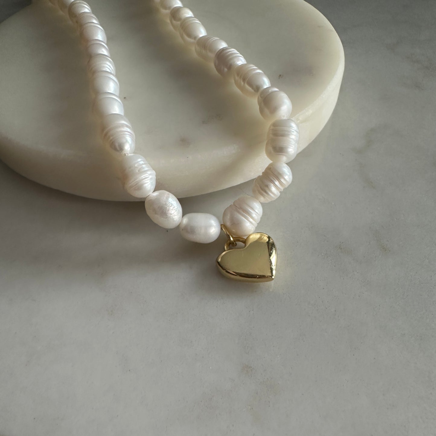 Pearl necklace with a gold heart charm on a marble surface