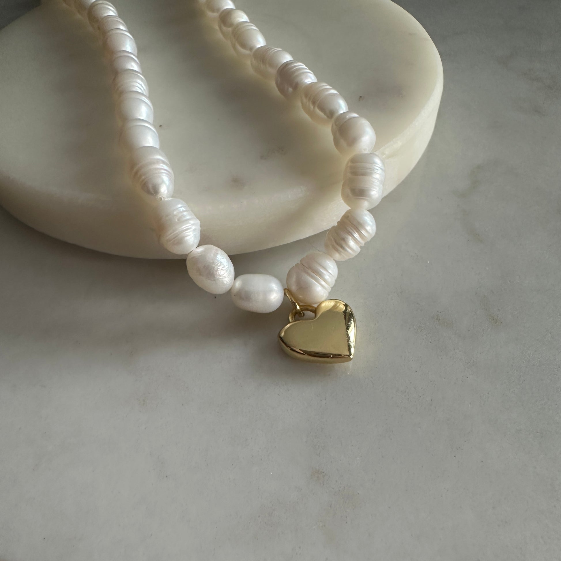 Pearl necklace with a gold heart charm on a marble surface