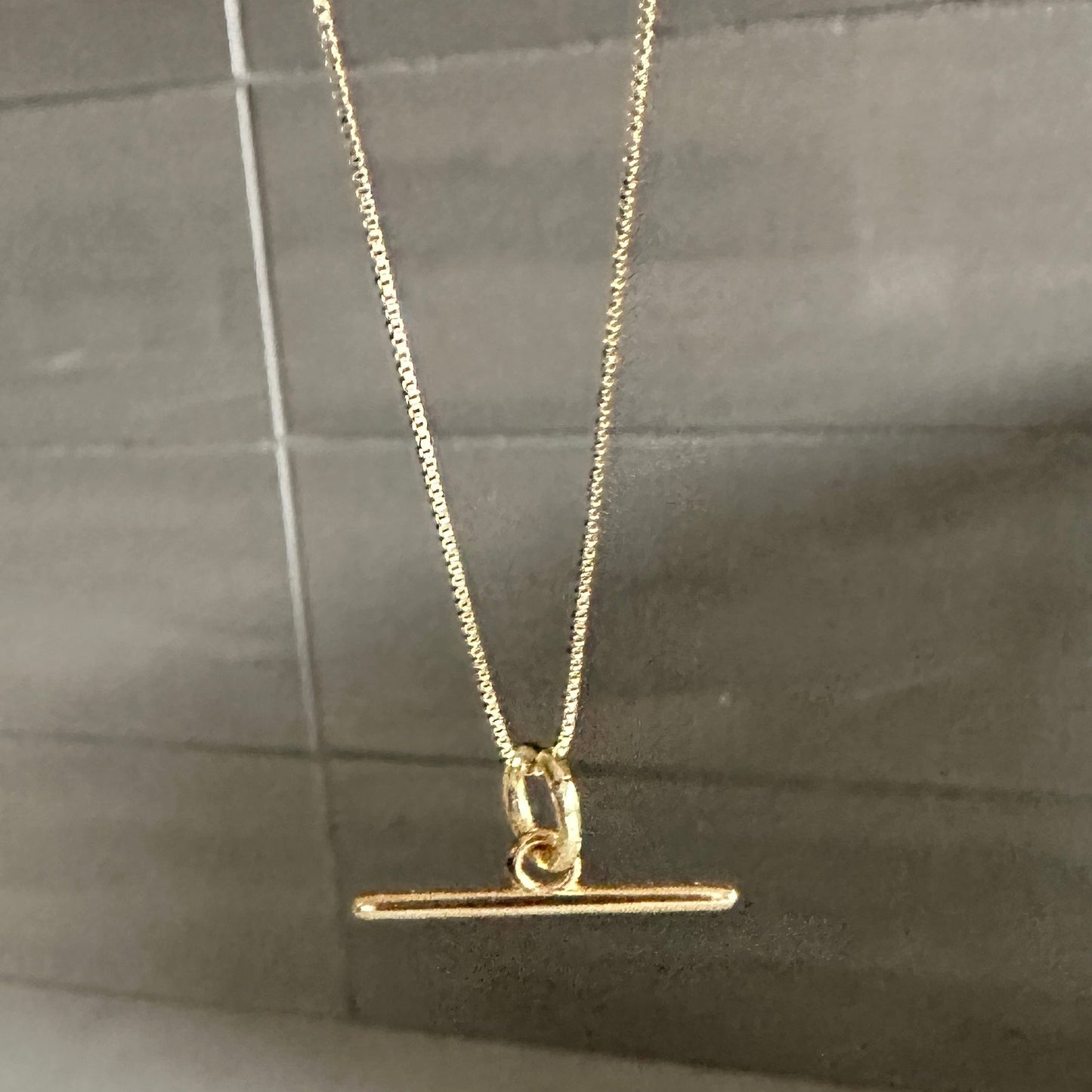 Gold necklace with a T-bar pendant on a gray surface