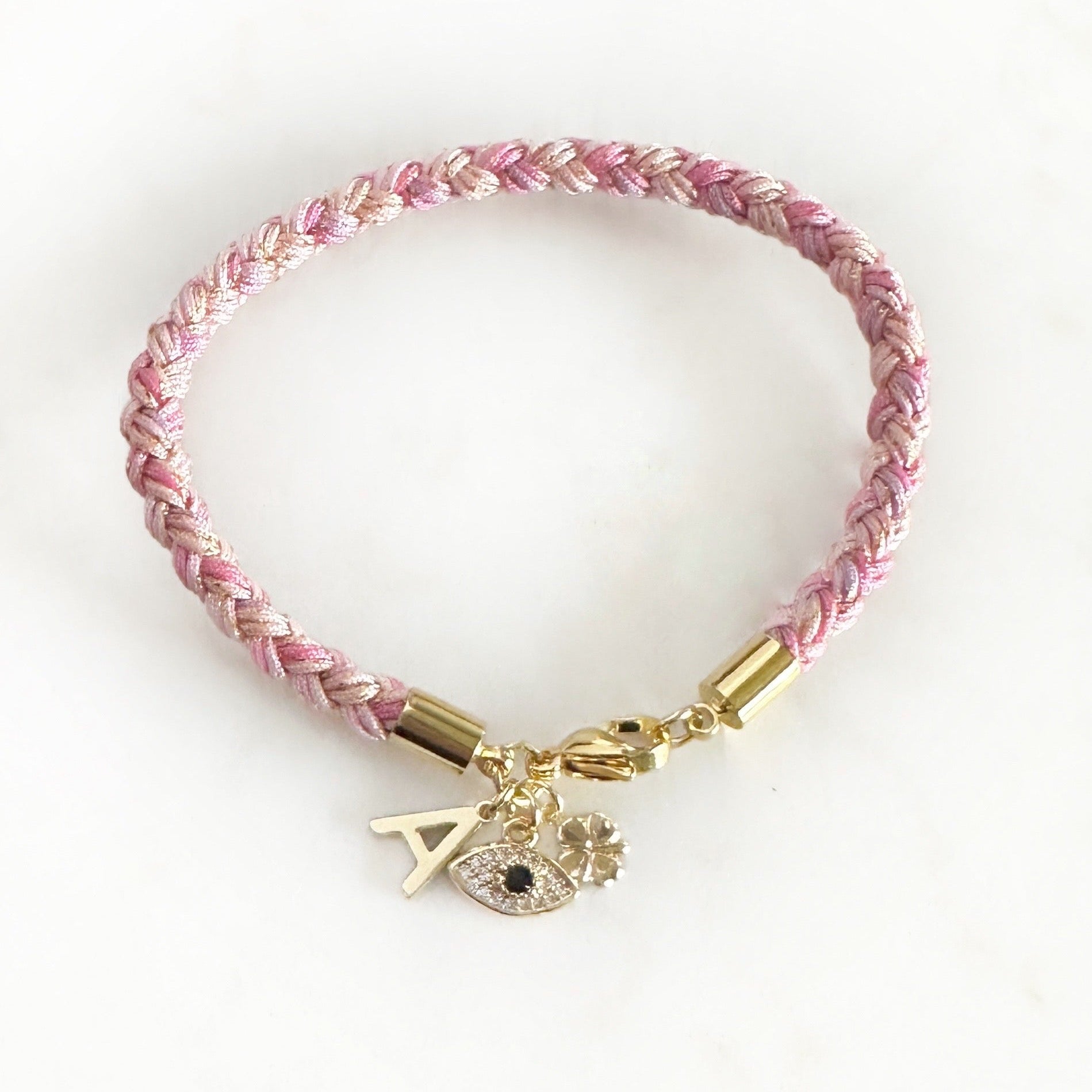 Pink braided bracelet with gold accents and charms on a white background