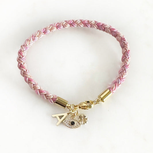 Pink braided bracelet with gold accents and charms on a white background
