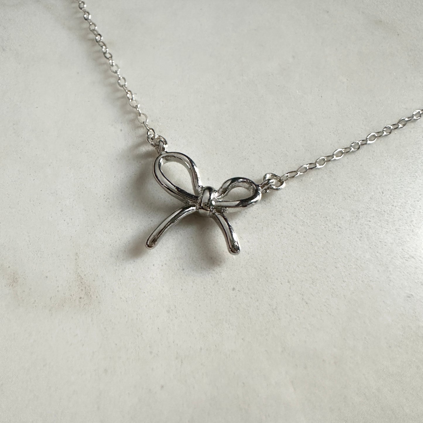 Silver bow-shaped pendant on a chain against a light gray background