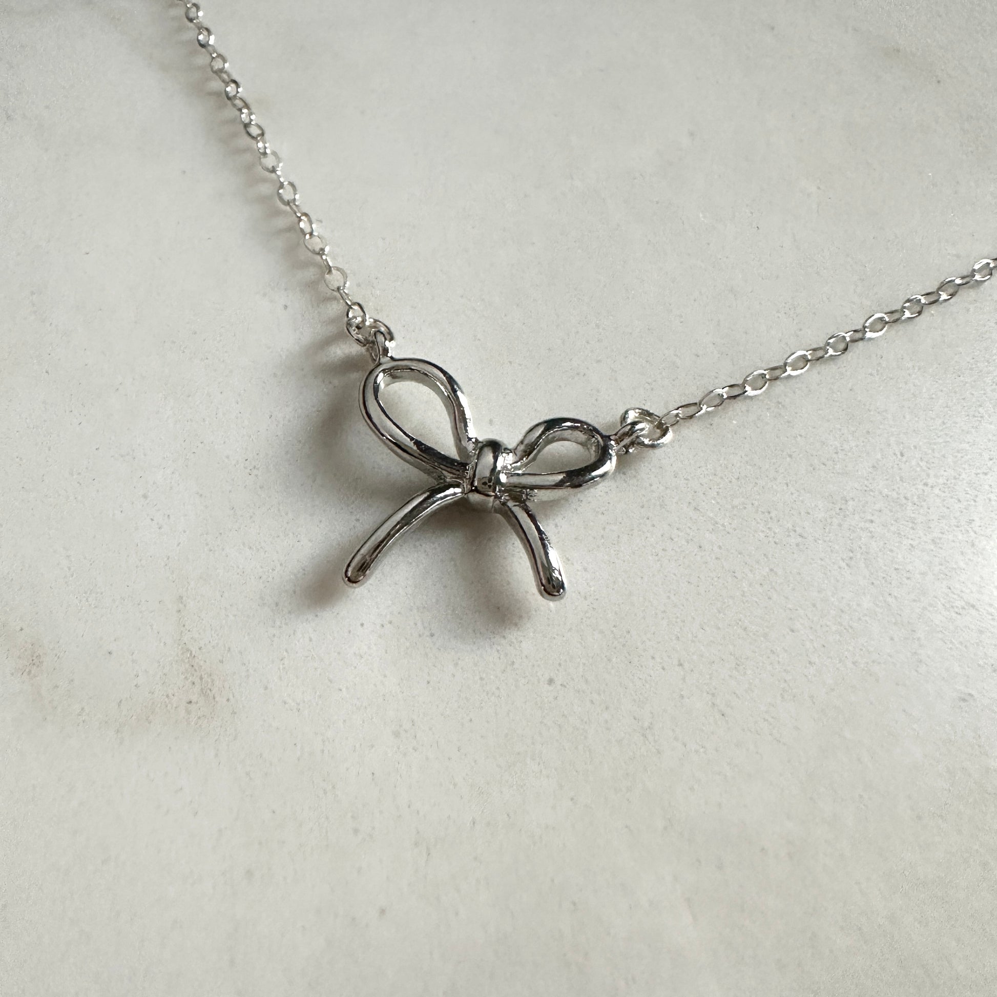 Silver bow-shaped pendant on a chain against a light gray background