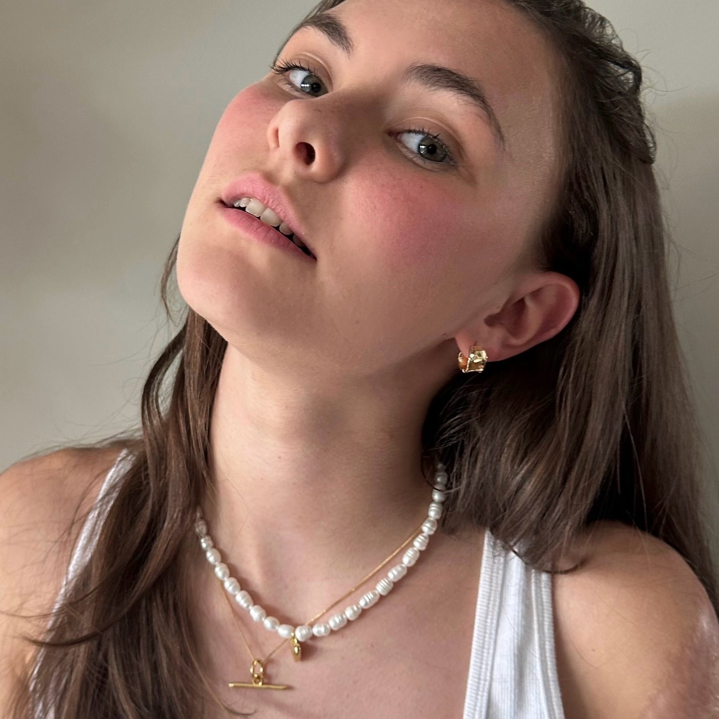 Woman wearing a pearl necklace and gold earrings against a neutral background