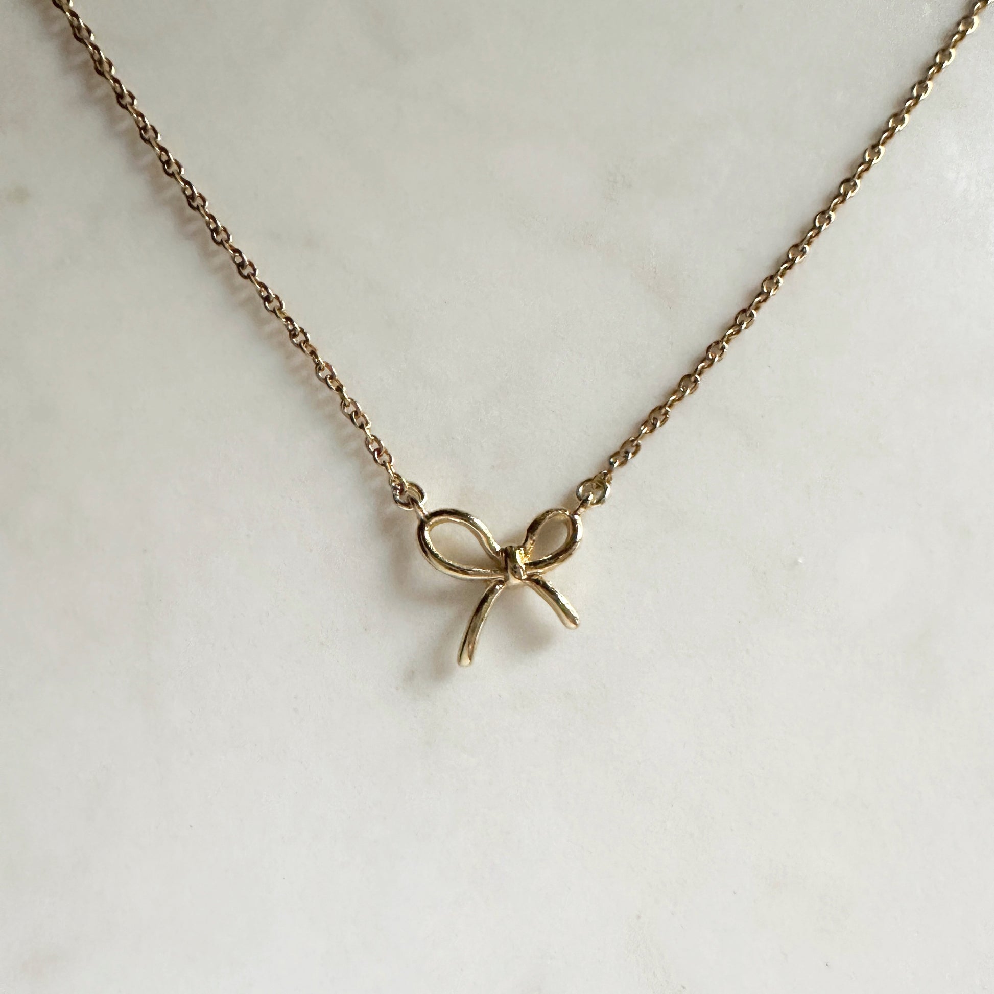 Gold bow-shaped necklace on a light background