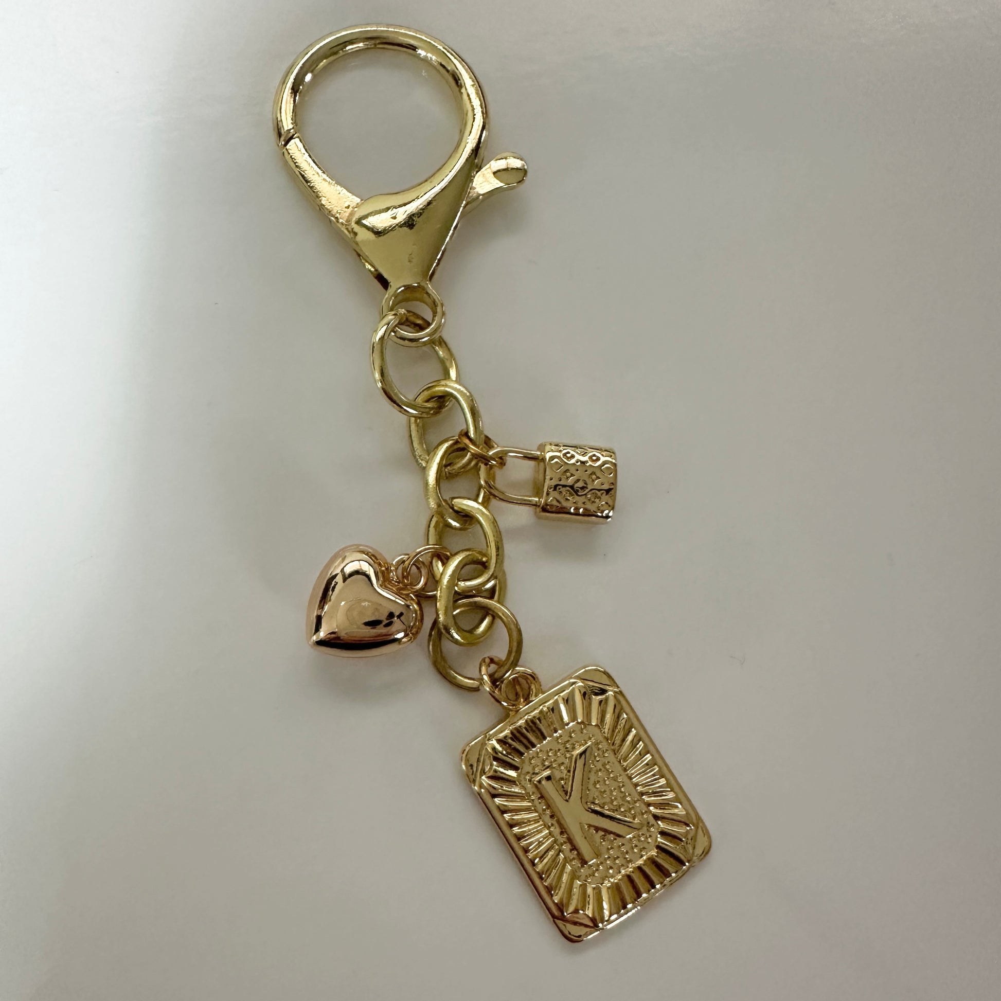 Gold keychain with heart and square charm on a light gray background