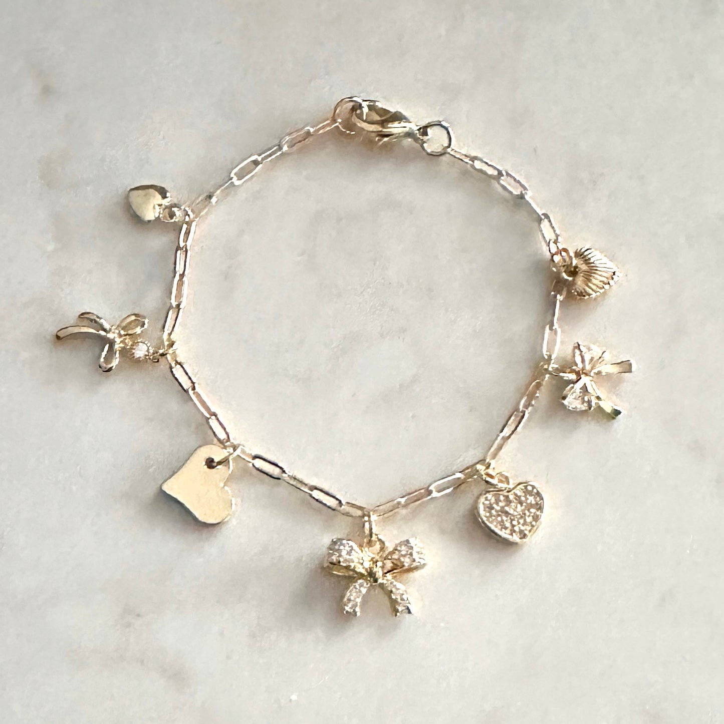 Gold bracelet with various charms on a light marble background