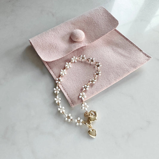 Pearl bracelet with a heart charm on a pink jewelry pouch on a light marble background