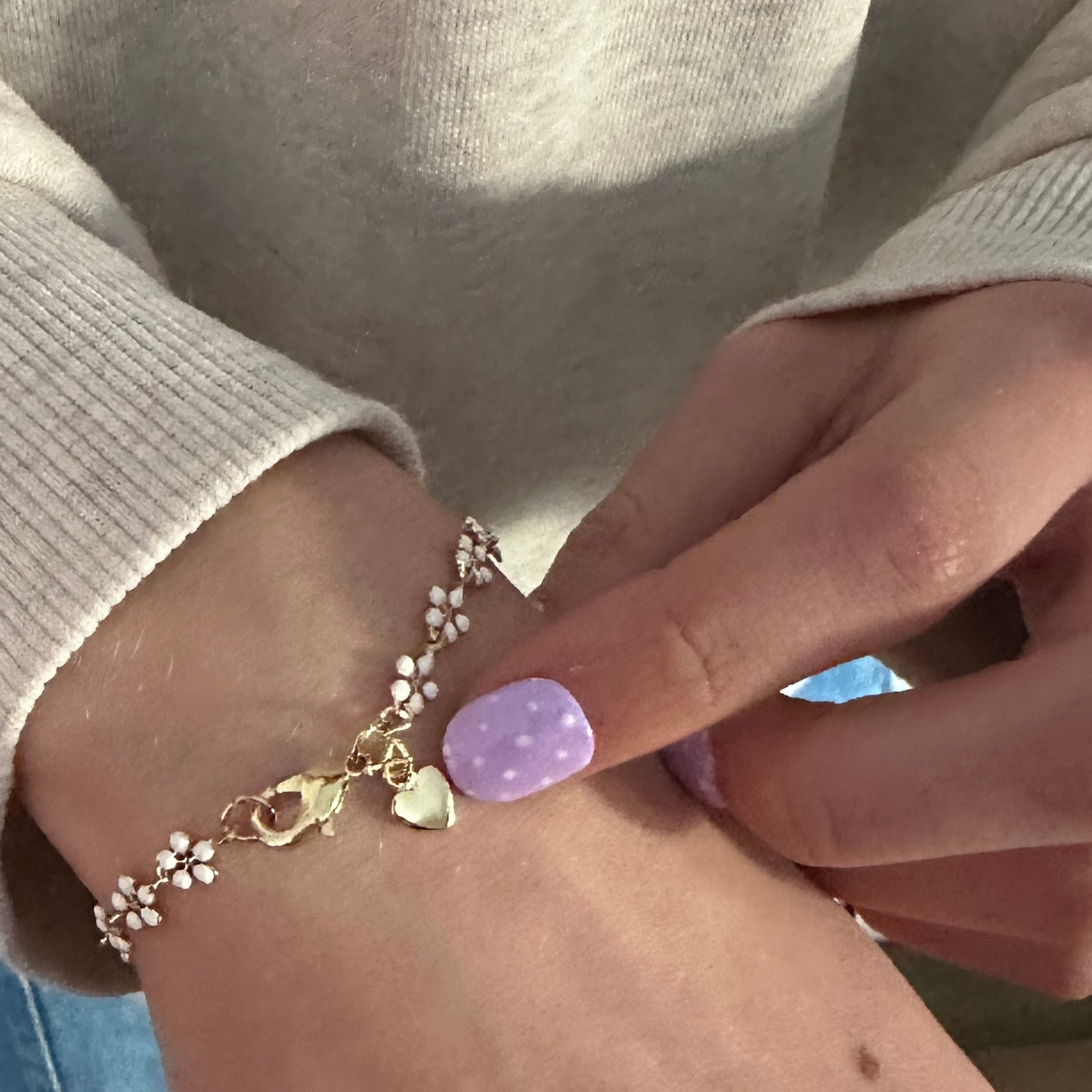 Close-up of a wrist wearing a delicate bracelet with heart and flower charms.