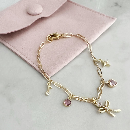 Gold bracelet with charms on a light pink fabric background
