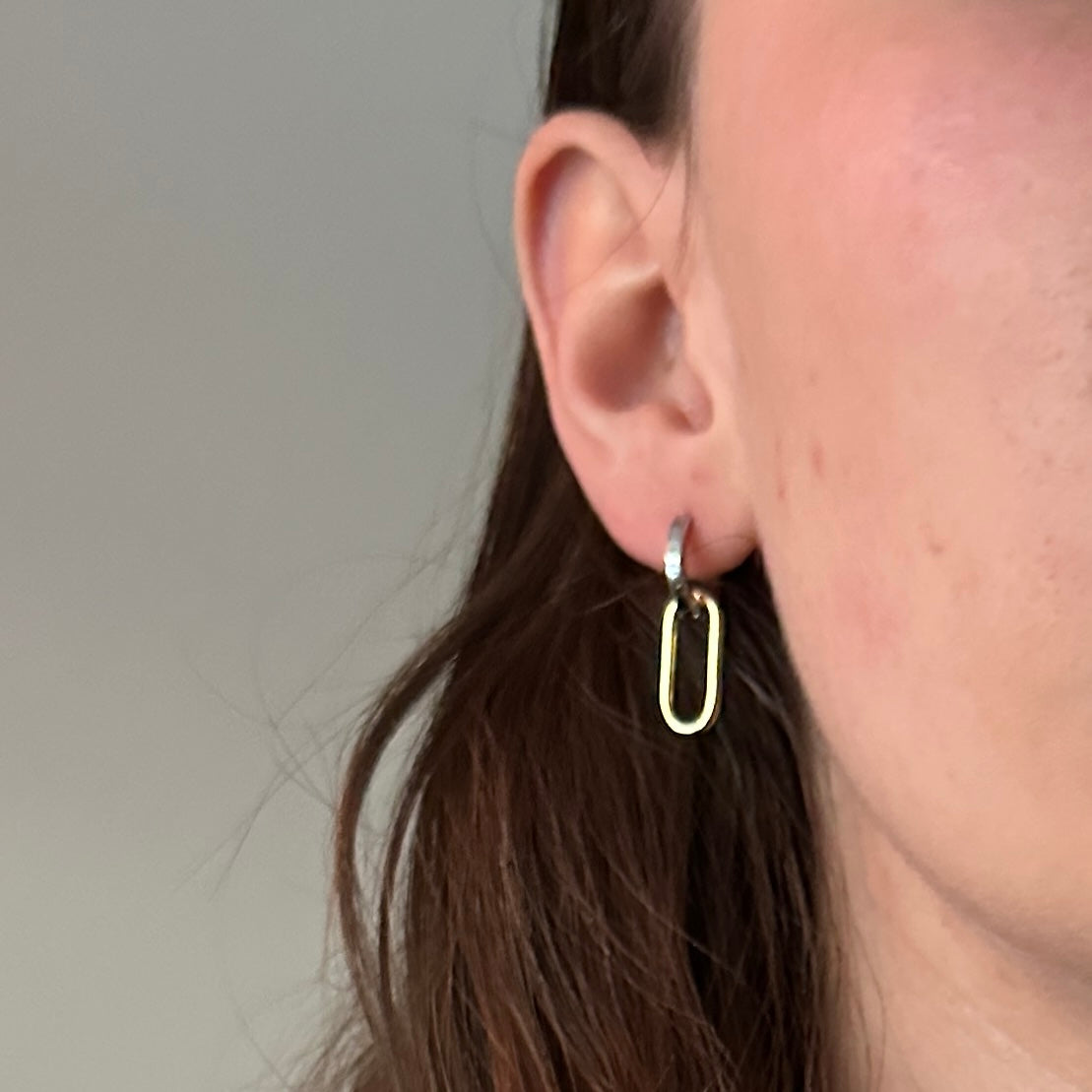 Close-up of an ear wearing a gold hoop earring against a neutral background