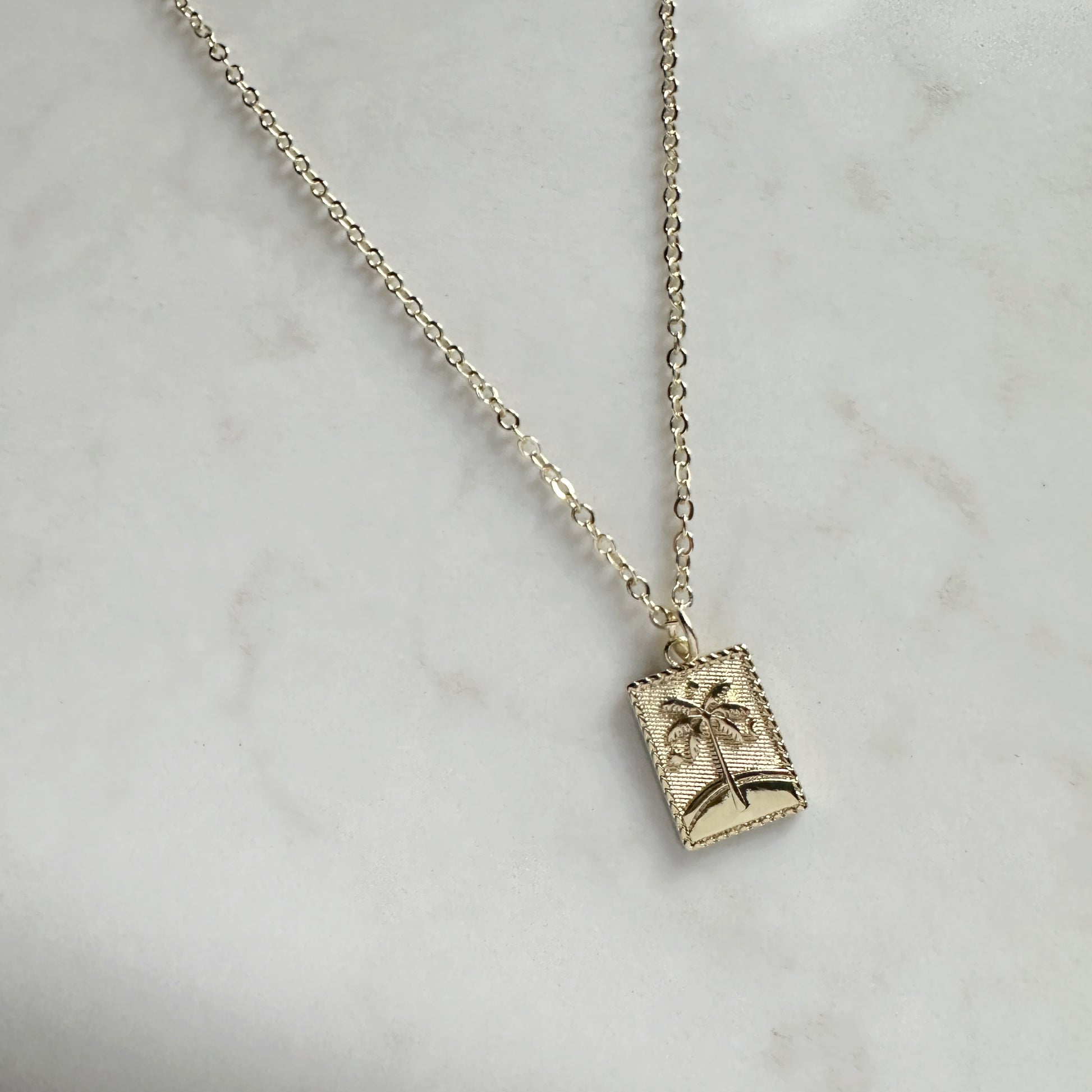 Necklace with a pendant featuring a palm tree design on a marble surface