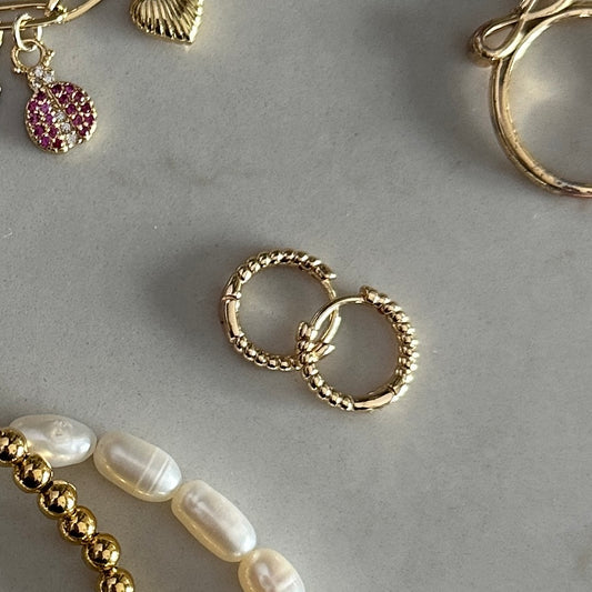 Gold hoop earrings on a gray surface with other jewelry items.