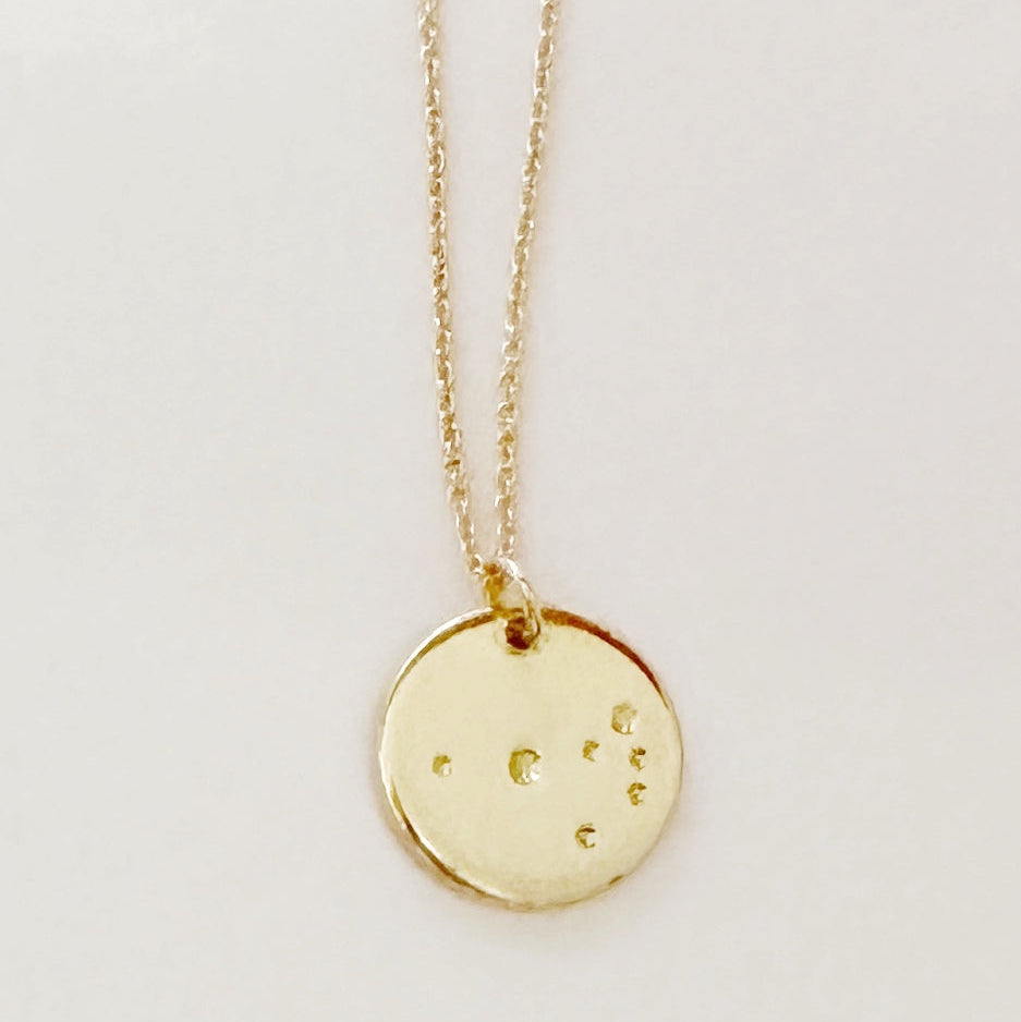 Gold necklace with a round pendant on a light gray background