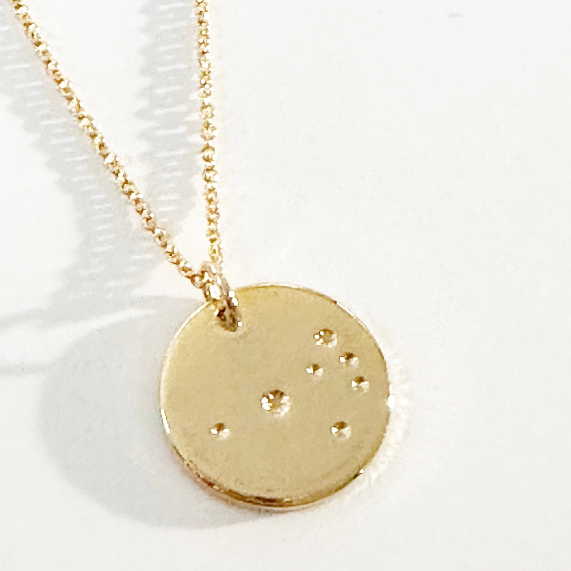 Gold necklace with a circular pendant featuring constellations on a white background