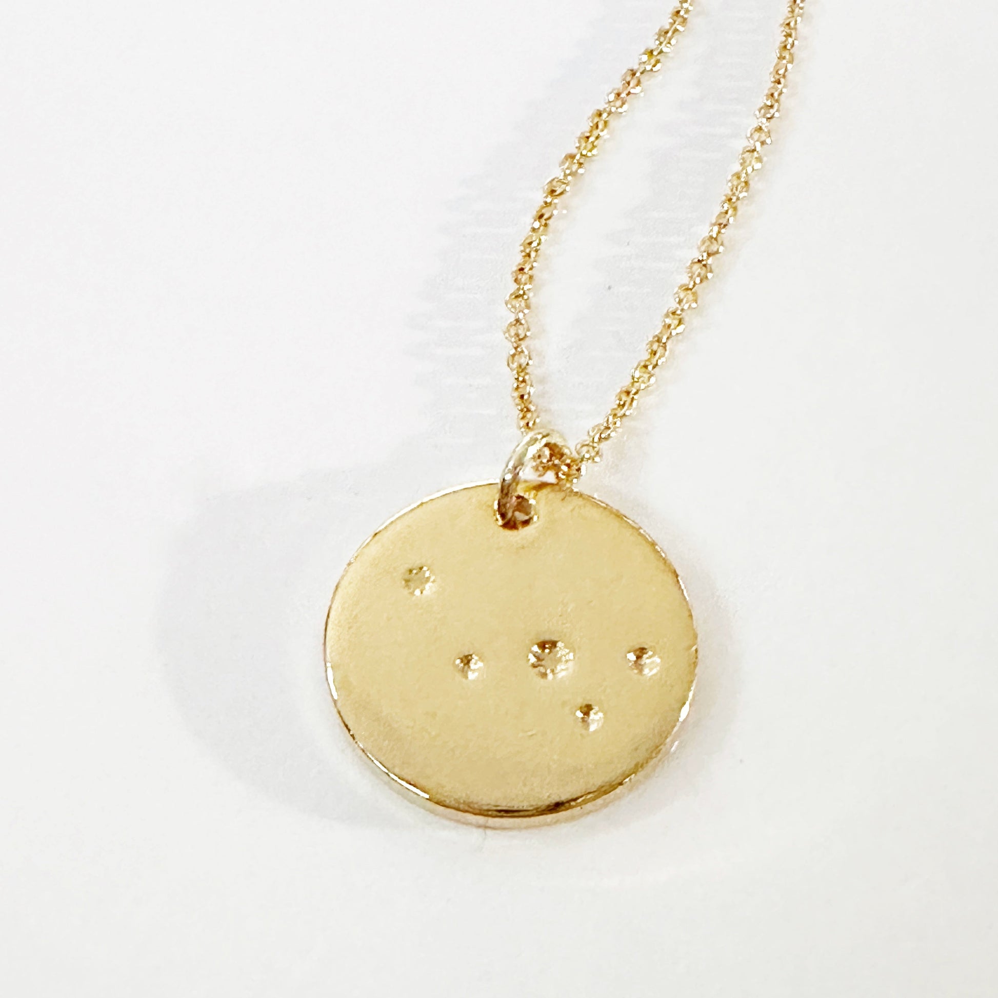 Gold necklace with a round pendant featuring star constellations on a white background