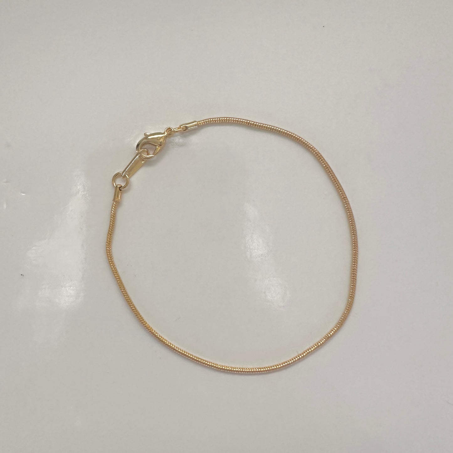 A delicate gold snake chain bracelet with a lobster clasp, displayed on a plain white surface.
