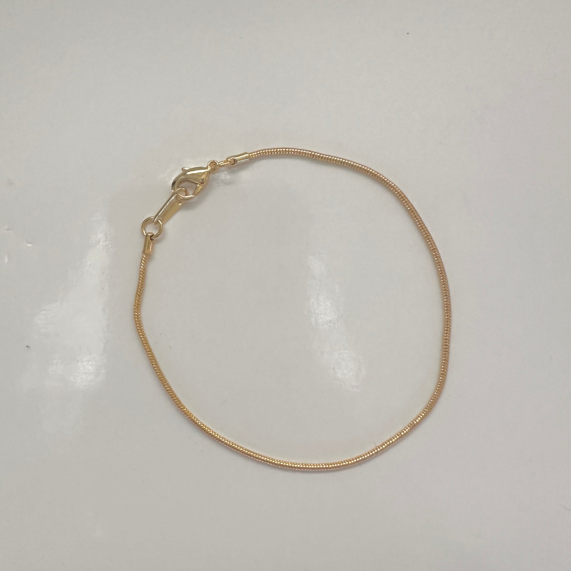 A delicate gold snake chain bracelet with a lobster clasp, displayed on a plain white surface.