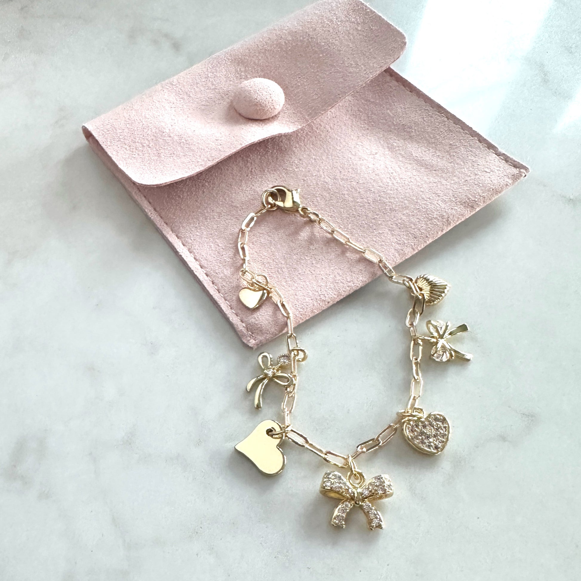 Gold bracelet with charms on a pink velvet pouch on a marble surface