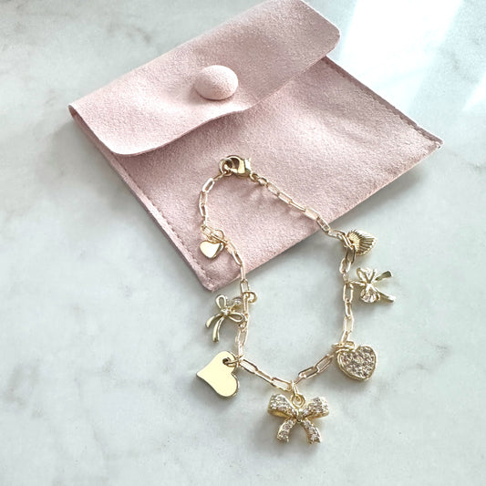 Gold bracelet with charms on a pink velvet pouch on a marble surface