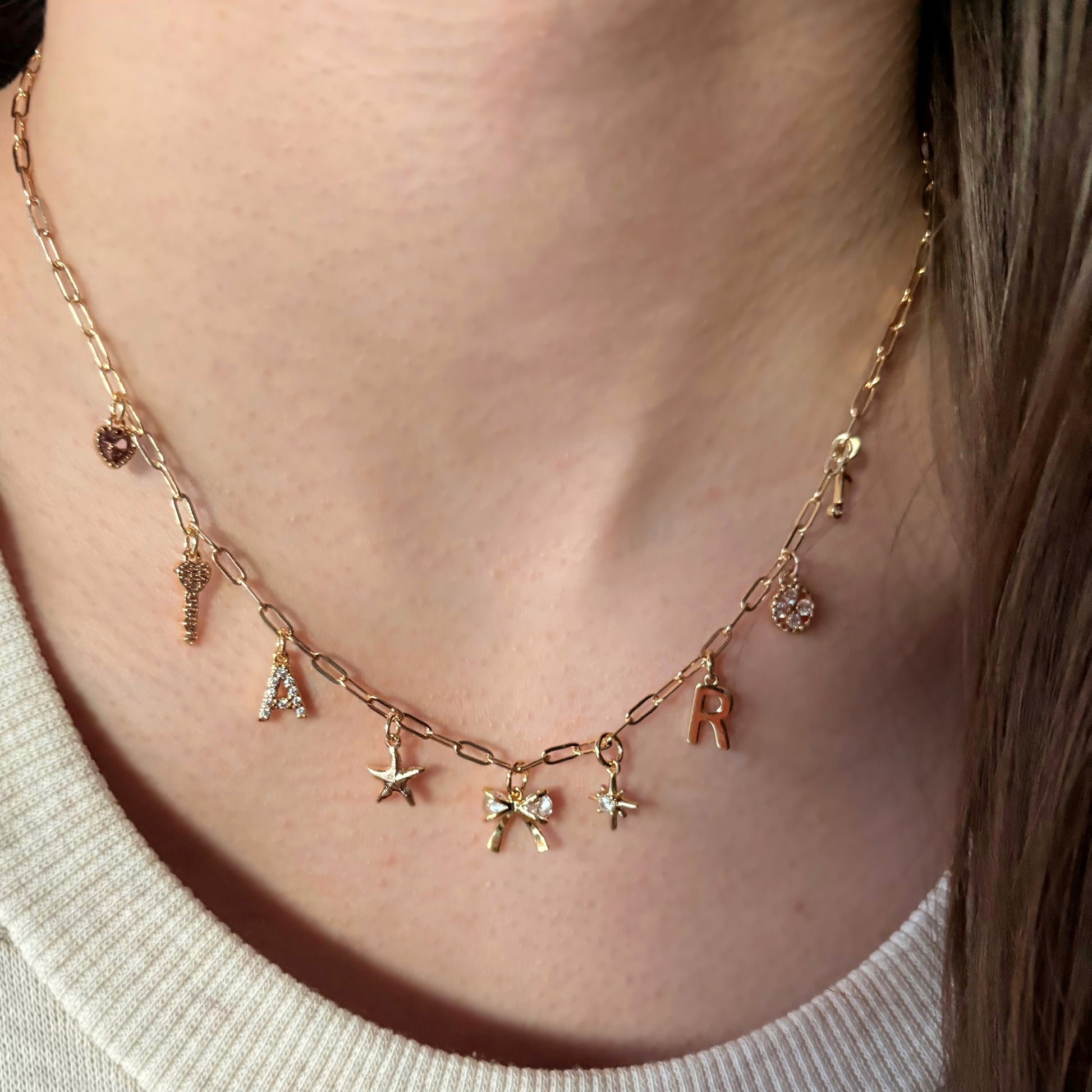 Gold necklace with various charms on a person wearing a white sweater.