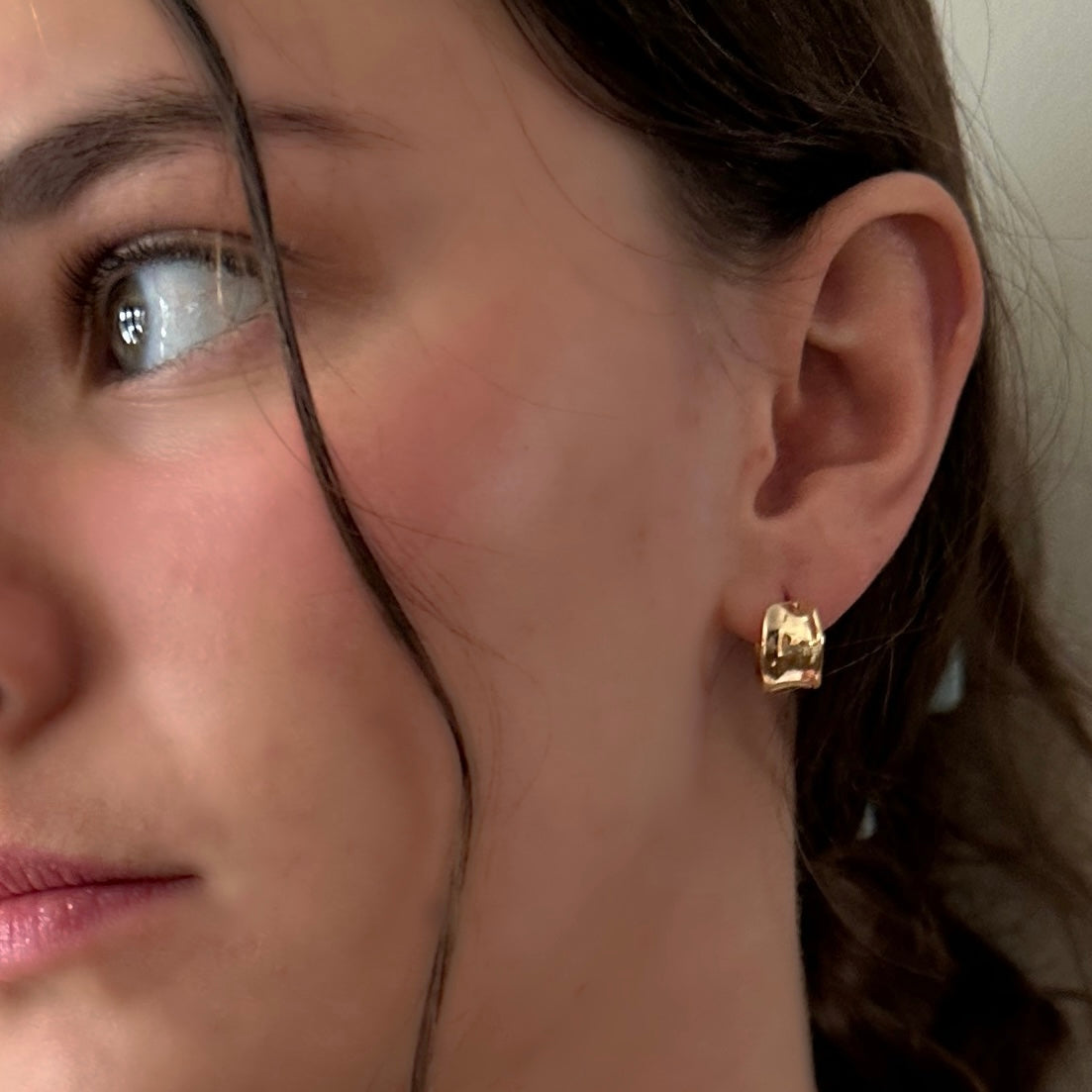 Close-up of a person wearing a gold hoop earring.