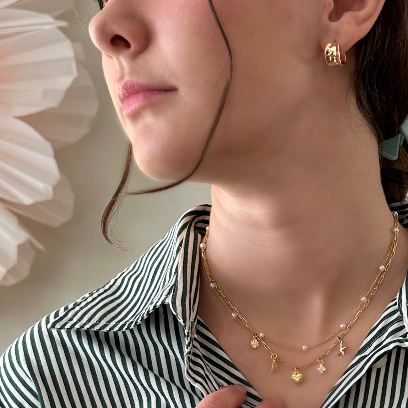 Close-up of a person wearing a gold necklace with small pendants against a neutral background.